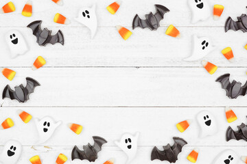 Halloween frame of candy corn and spooky chocolate ghosts and bats. Top down view over a white wood...