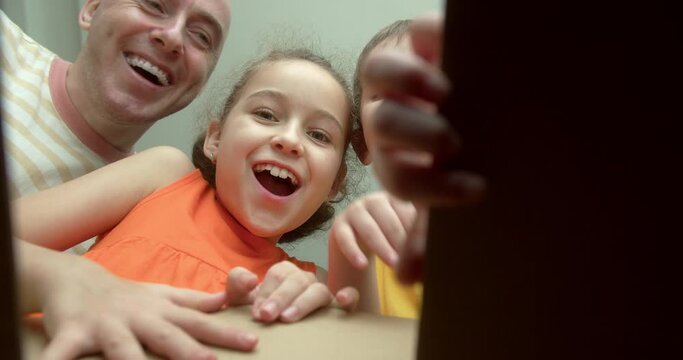 Happy dad and his Children, overjoyed at the surprise, open a box with gifts. Little children, girl and a brother, look in a cardboard box. Inside view. Children pull their hands into the box.