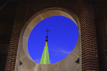 Round portal opening with weather church steeple, green  patina and cross. View from inside, with red bricks and stone.
