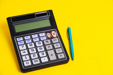 Calculator turned off and a ballpoint pen on yellow background.