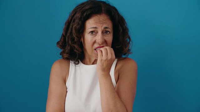 Middle age woman standing with nervous expression over isolated blue background