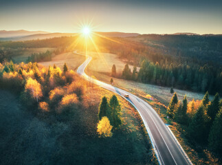 Aerial view of mountain road in autumn forest at sunset in Ukraine. Top view from drone of road in...