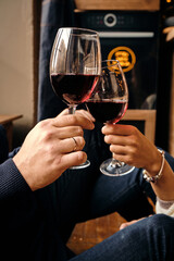 Glasses of red wine in the hands of a girl and a man who are resting. Celebrate and enjoy the moment. Tasting of alcoholic beverages. Romantic evening aperitif