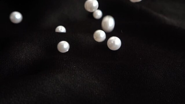 White pearls fall on black fabric. Slow motion.