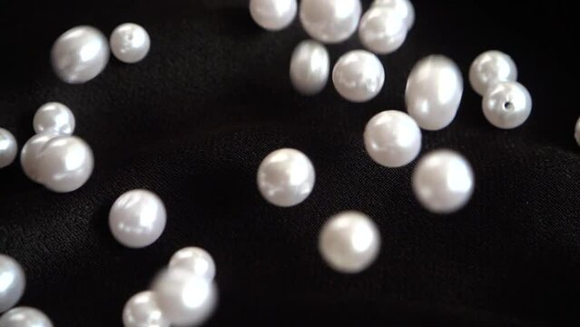White pearls fall on black fabric. Slow motion.