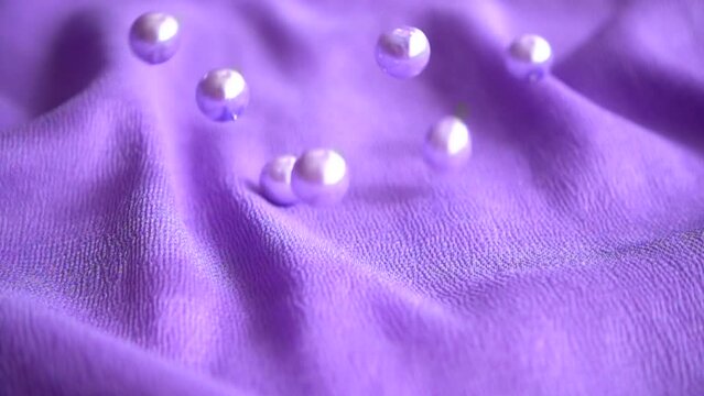 Pearls fall on a blue cloth. Slow motion.