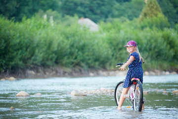 A girl rides a bicycle in the countryside. A small clean river.