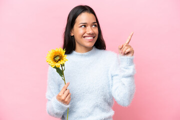 Young Colombian woman holding sunflower isolated on pink background pointing up a great idea