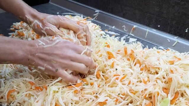 Woman kneads sauerkraut with carrots on the table.