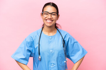 Young nurse Colombian woman isolated on pink background posing with arms at hip and smiling