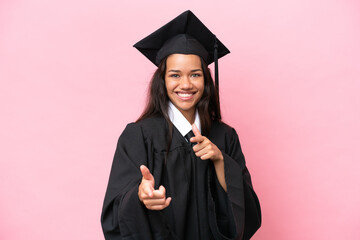 Young university Colombian woman graduate isolated on pink background pointing to the front and smiling
