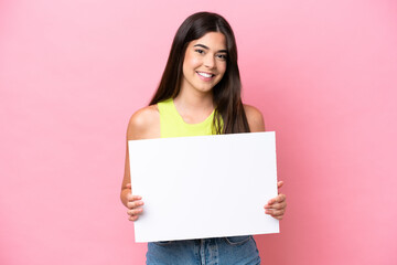 Young Brazilian woman isolated on pink background holding an empty placard with happy expression
