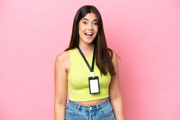 Young Brazilian woman with ID card isolated on pink background with surprise facial expression