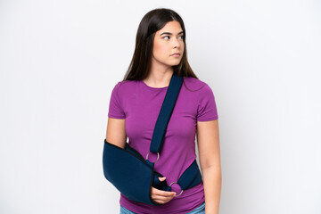 Young Brazilian woman with broken arm and wearing a sling isolated on white background looking to...