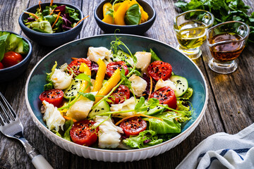 Fish salad - fried halibut fillet with fresh vegetables on wooden table
