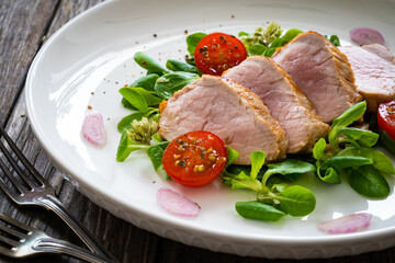 Fried pork loin with fresh vegetables on wooden table
