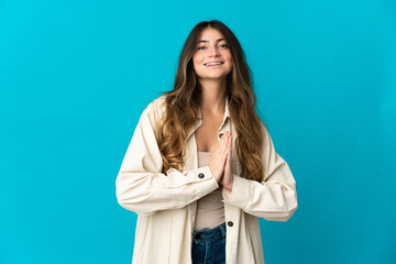 Young caucasian woman isolated on blue background keeps palm together. Person asks for something