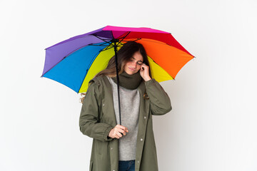 Young caucasian woman holding an umbrella isolated on white background frustrated and covering ears