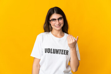 Young volunteer woman isolated on yellow background inviting to come with hand. Happy that you came