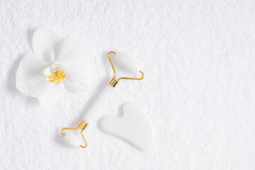 White jade roller and gua sha tool, orchid flower on white towel background. Flatlay of gua sha...