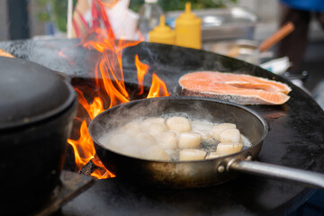 Process of cooking scallop meat, salmon on black brazier at summer outdoor food market: close up....