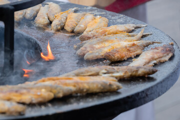 Crispy breaded european smelt fish on black brazier at summer outdoor food market: close up....