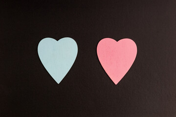 two wooden heart symbols on a black background, hearts at a distance from each other