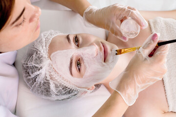 A beautician applies a mask to the skin of a woman's face for therapeutic purposes. Rejuvenation, acne treatment