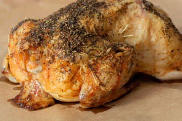 Whole chicken coated in mixed herbs roasted in an oven. On a brown paper background