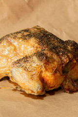 Whole chicken coated in mixed herbs roasted in an oven. On a brown paper background