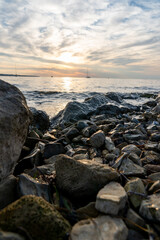 Fototapeta na wymiar Sonnenuntergang am Meer mit Segelbooten im Hintergrund und Steinen im Vordergrund