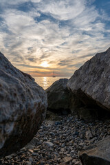 Sonnenuntergang am Meer mit Segelbooten im Hintergrund und Steinen im Vordergrund