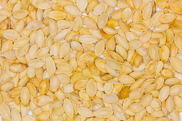 Dried pumpkin seeds in husks. Yellow pumpkin seeds. Wallpaper, background. Flat oval seed of squash. Edible seed of a pumpkin. Healthy food. Natural product. Roasted snack. Pepita. Top view. Close-up