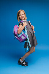 Back to school. A schoolgirl with a school bag on an isolated blue studio background. a little girl is holding a backpack.