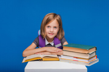 The little schoolgirl raised her hand to answer the question. a schoolgirl with books on a blue background.