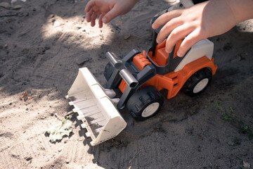 Fototapeta na wymiar A toy orange tractor in the hands of a boy. A little boy is playing with a plastic bulldozer