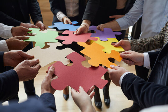 Business team trying to find creative solutions to problem. Group of people connecting different red, yellow, orange, green, blue and purple jigsaw puzzle pieces. Cropped close up. Teamwork concept
