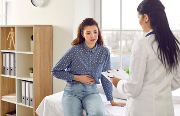 Female medical specialist consults young female patient who complains of abdominal pain. Woman experiences abdominal discomfort due to menstrual pain, pancreatitis, gastritis or diarrhea.