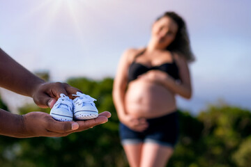 interracial couple holding shoes expecting pregnant baby.