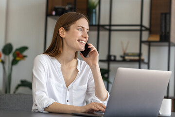Young business woman working in the modern office talking on the phone while sitting at the...