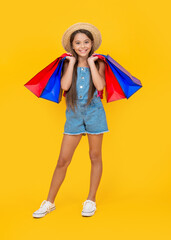 happy teen child with purchase bags on yellow background. full length