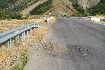 Highway with deformed spot near traffic barrier built in countryside near giant mountains and...