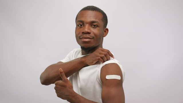 Young man shows thumb-up demonstrating vaccination patch on arm in white studio