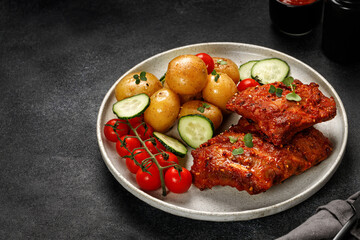 Plate with Marinated pork bbq ribs, young potatoes, tomatoes on black  dark background. Hearty Dinner, lunch, meal. Copy space, place for text.