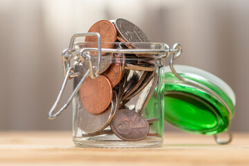 An open jar with small coins stands on a wooden table on a neutral background, close-up, selective focus. A concept for business and finance, savings and price increases.