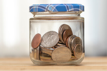 A closed jar with small coins of American cents on a wooden table, close-up, selective focus. A concept for business and finance, savings and price increases.