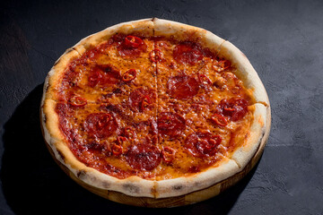 Pizza with tomato sauce, mozzarella, salami, chili, honey on black background. View from above