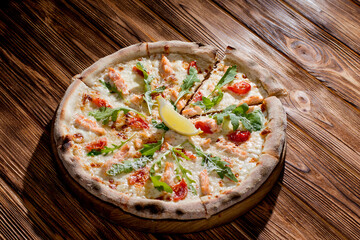 Pizza with salmon, mozzarella, cherry tomatoes, arugula, lemon and parmesan. Italian cuisine on a...