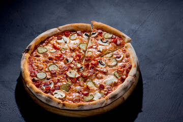 Appetizing pizza with hunting sausages, mozzarella cheese, pickled cucumbers, chili peppers on a tomato base on black background