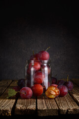 ripe plums in a transparent glass jar on a wooden table on a dark background. rustic still life with copy space